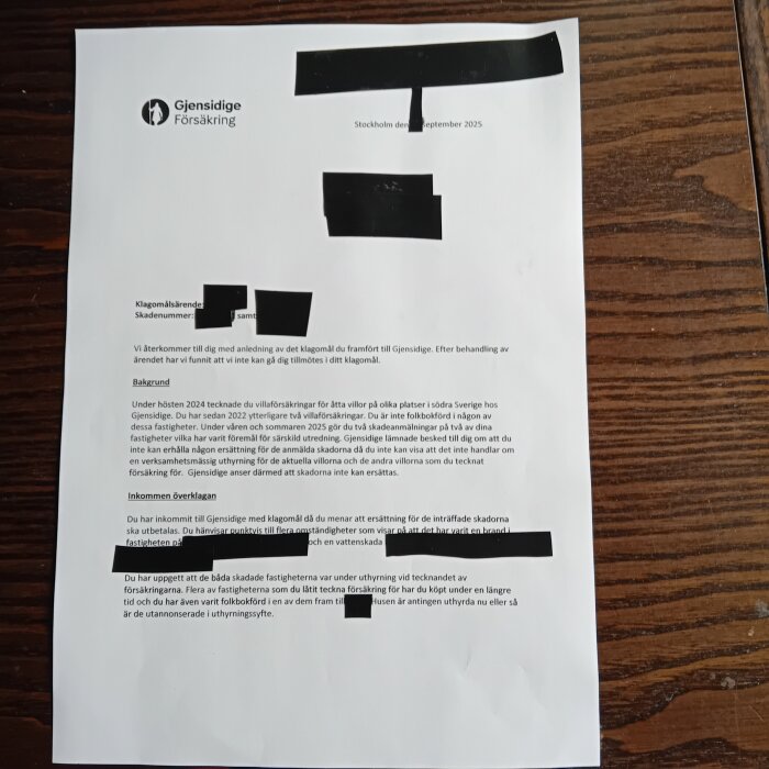 Ett dokument från Gjensidige Försäkring med text och delar markerade med svart för att dölja information. Dokumentet ligger på ett träbord.