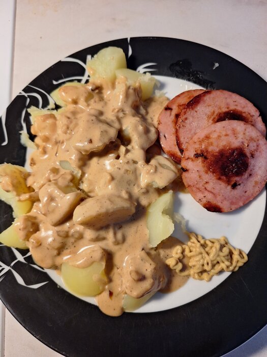 Tallrik med kokt potatis, löksås, stekt falukorv och en klick senap.