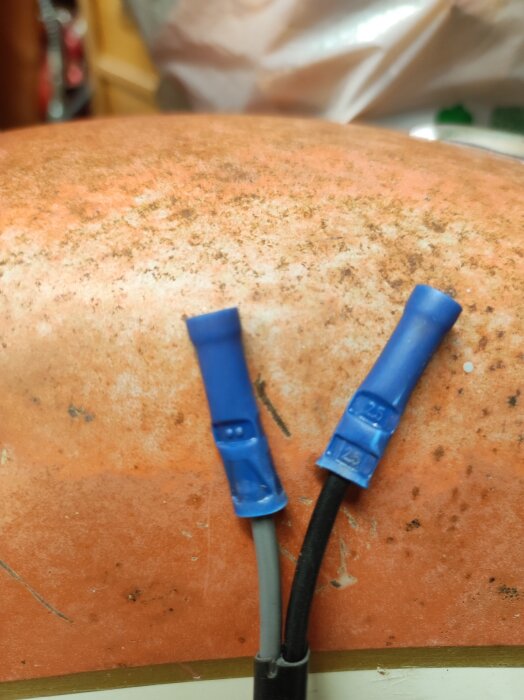 Blå kabeländhylsa från Biltema till vänster och elpress hylsa med stämplade siffror till höger, liggande på en orange yta.