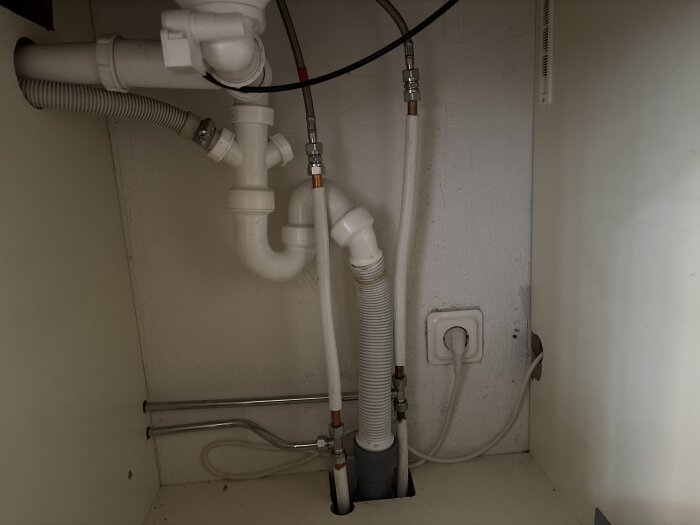 Rör och avlopp under diskbänk med anslutningar för diskmaskin och möjlig installation av tvättmaskin.