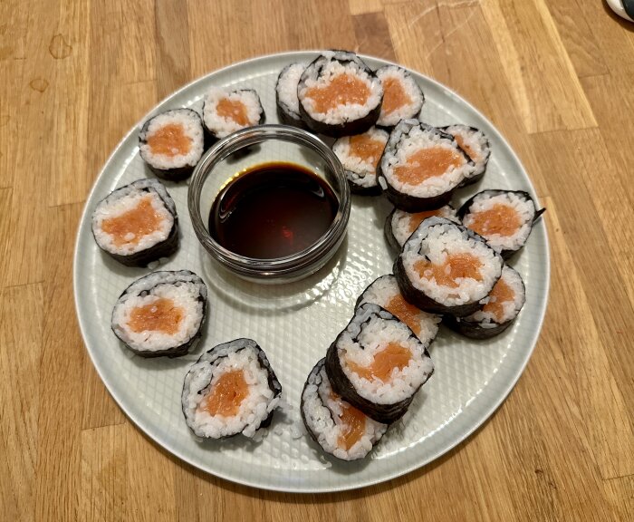 Sushibitar med lax och ris på en tallrik, med en skål sojasås i mitten.