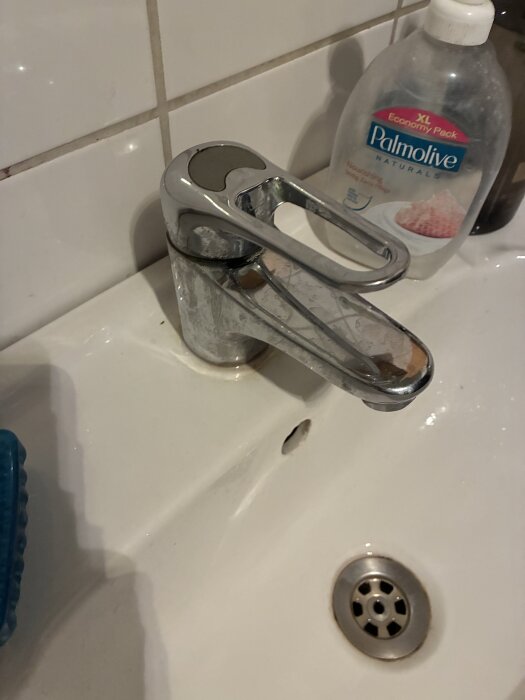 Kromad engreppsblandare i badrum med synlig läcka vid basen, tillsammans med handtvålflaska och diskho.