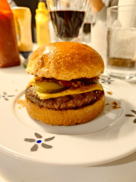 Hamburgare med ost och pickles på en tallrik, omgiven av ketchup, senap, ett glas rödvin och vatten.