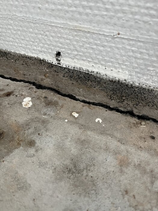 Golvbild med synlig glipa mellan betong och vägg, främst i hörn. Lite smuts och skador på väggen. Frågor kring ventilation eller behov av fogning.