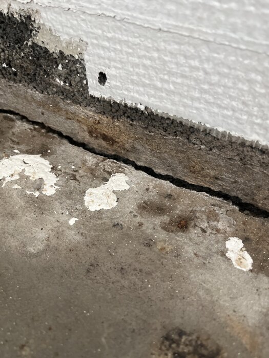 Spricka mellan golv och vägg med slitage och färgskador, möjligen för ventilation, i rum under renovering.