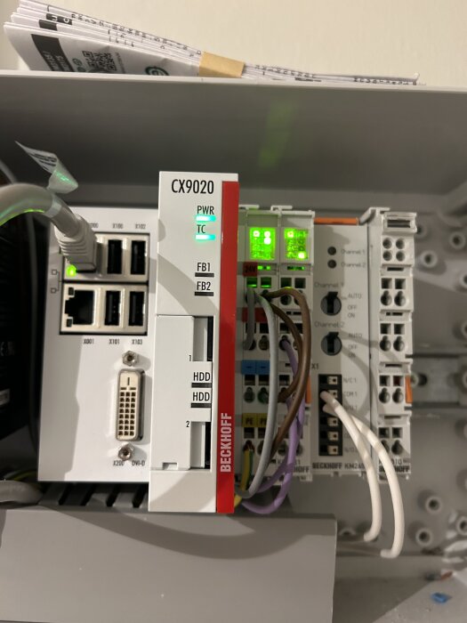 Beckhoff CX9020 PLC med anslutna kablar och lysande indikatorer, används för att optimera elförbrukning och belysning i ett hemautomationssystem.