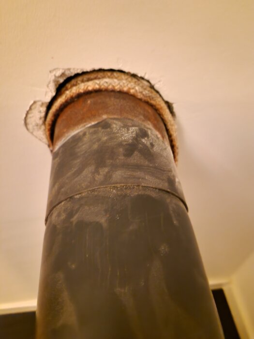 Kaminrör som går genom taket, tätat med tätningsgarn, ses underifrån i behov av återmontering efter rumsrenovering.