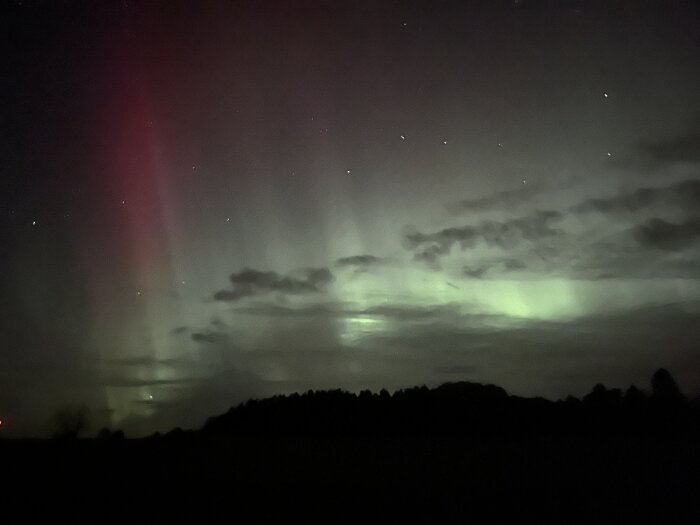 Norrsken över mörk landskapssiluett, gröna och röda ljussken på natthimlen med stjärnor.
