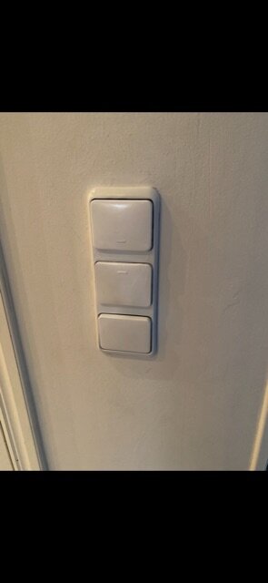 Tre vita strömbrytare på en vägg, eventuellt inkluderande dimmers för belysning, diskussion om estetisk utformning och funktionalitet av knapparna.