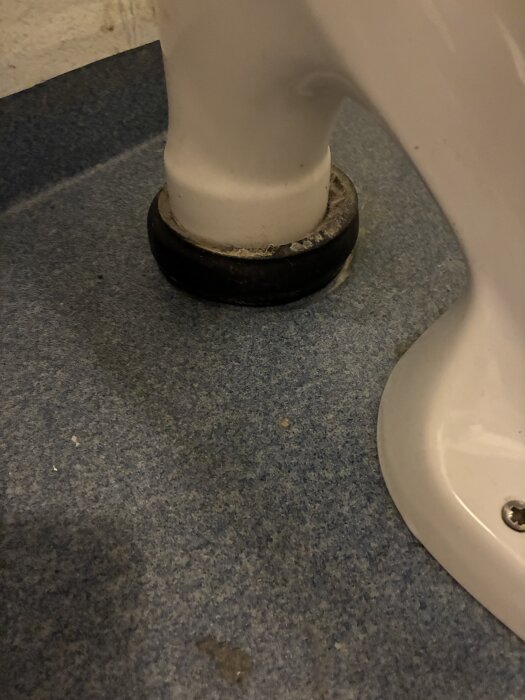 Närbild av en toalettstol med en svart manschett vid basen på ett blått golv.