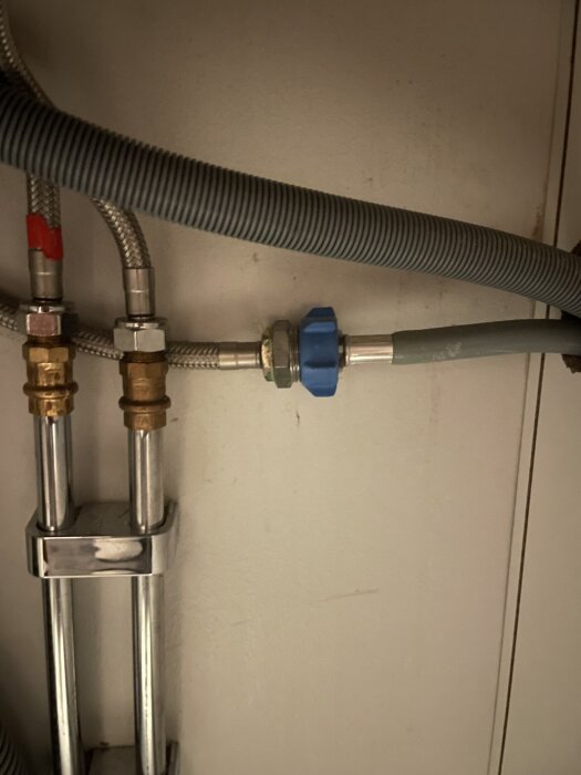 Blå mutter på en vattenanslutning under en inbyggd tvättmaskin, omgiven av slangar och rör i ett skåp.