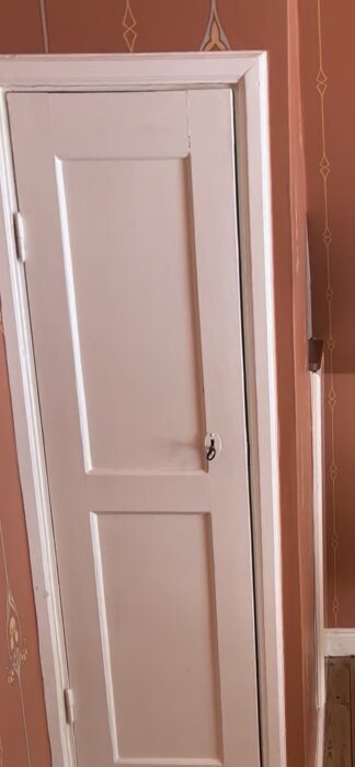 Vit garderobsdörr med enkel spegelprofil och "pärla", typiskt för 20-talshus, mot en röd vägg med dekorativa detaljer.