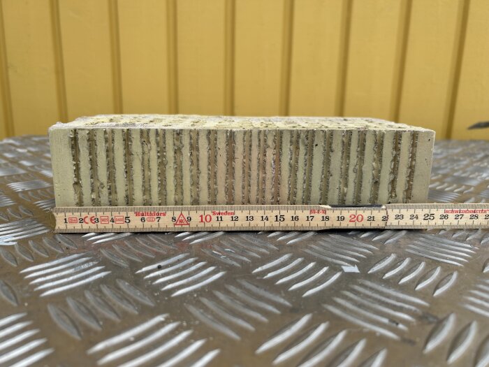 Tegelbit mot metallbakgrund med mätsticka som visar dess längd.