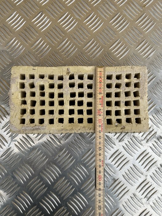 Tegelblock med hål och måttband på rutigt metallgolv.