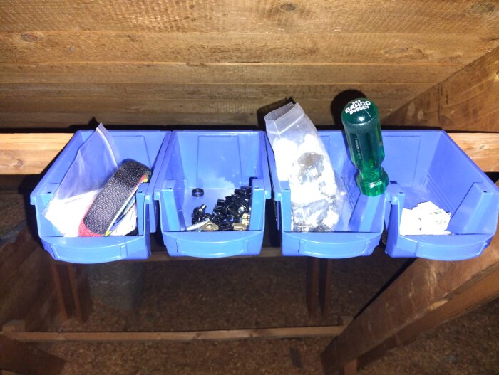 Blå plockbackar uppsatta på vinden, fyllda med kabelband, skruvar, en skruvmejsel och andra små komponenter för ett nätverksprojekt.