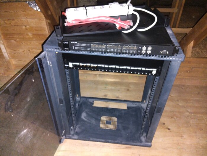 Ett nätverksrack med installerad utrustning på en vind, med kablar och switch synliga ovanpå.