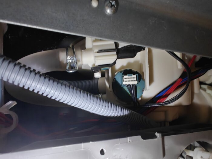 Inre komponenter av en Electrolux diskmaskin, inklusive slangar och kablar, syns genom en öppning i maskinens undersida.