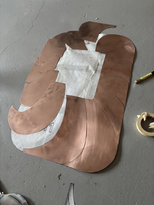 Kopparplåtar utskurna i olika former ligger på golvet, del av ett gnistskyddprojekt.