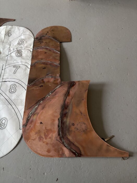 Kopparplåt i böjd form med lödningar och mönster bredvid en numrerad skiss.