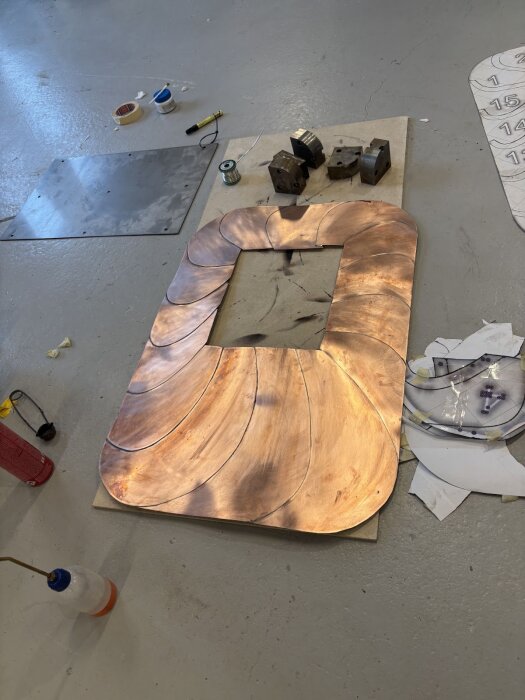 Kopparplåt med lödda skarvar placerad på golvet, omgiven av verktyg och material för lödning och bearbetning.