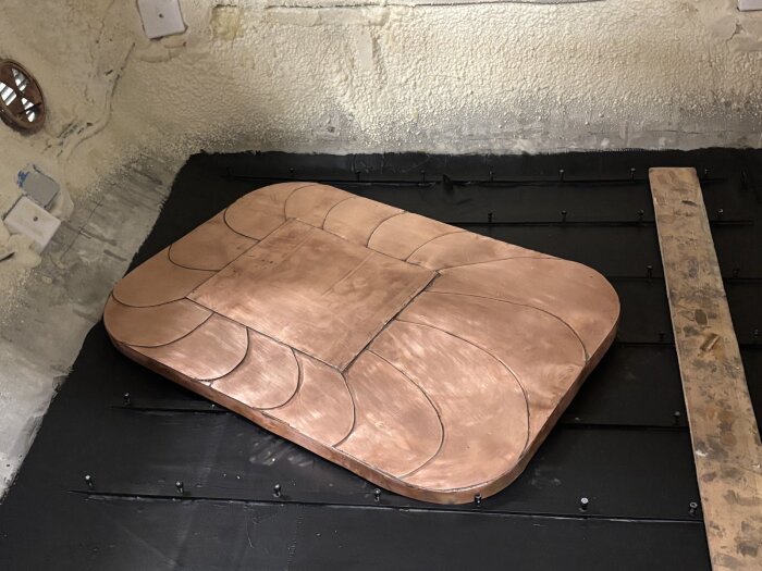 Kopparplåt monterad i vagnen, med lödade skarvar och mönster, omgiven av svarta material och träbit, del av ett gnistskyddsprojekt.