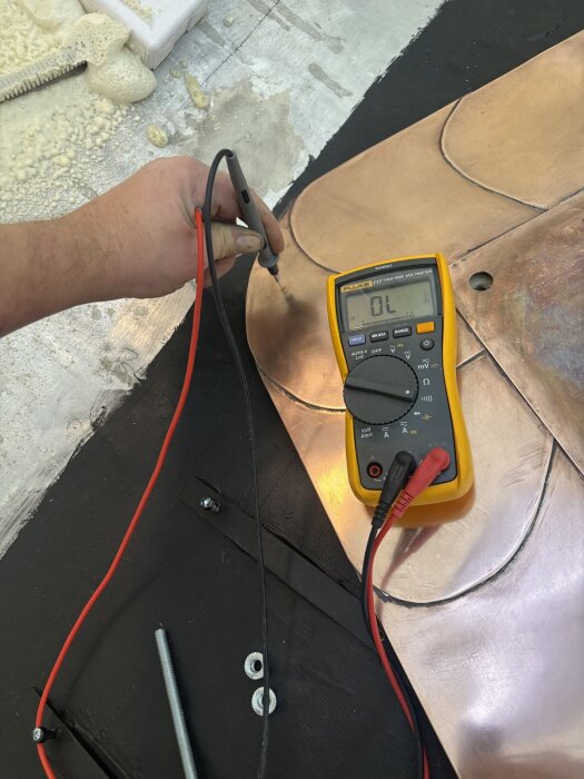 En person använder en multimeter för att mäta elektrisk isolering på kopparplåtar monterade på en svart yta.
