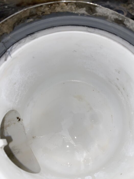 En närbild av en vit plastbehållare med en plastdel inuti, eventuellt del av en ventilations- eller avloppskomponent.