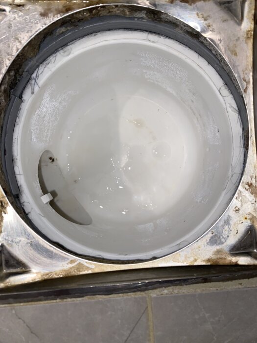 Öppet avlopp, del av VVS-installation, med synlig vit rörsektion och mindre smuts vid kanten, potentiell inspektionspunkt.