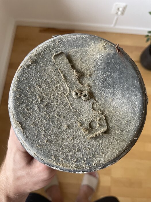 Ventilationslock med damm och vita prickar på ytan, fotograferat ovanifrån i ett rum med trägolv i bakgrunden.