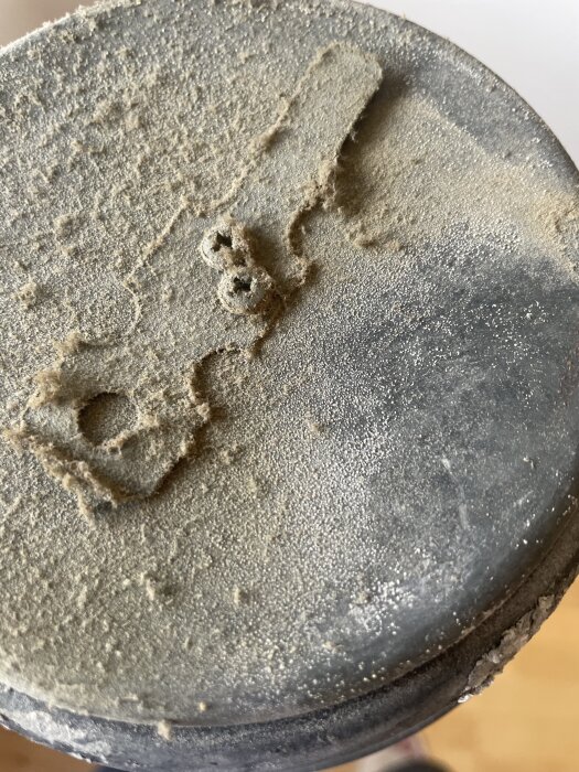 Detaljbild av en dammig och smutsig yta i ventilationen med otydliga mönster avlagringar.