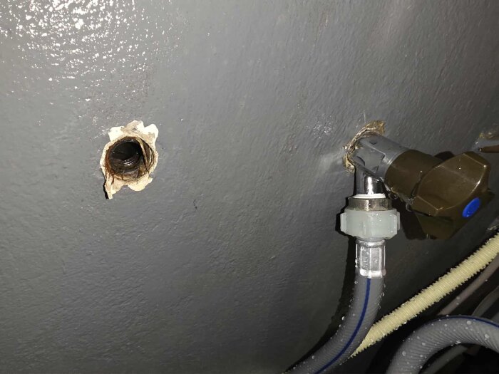 Uppmurat hål i en grå vägg med ett synligt rör och en fastmonterad ventil med ansluten slang.