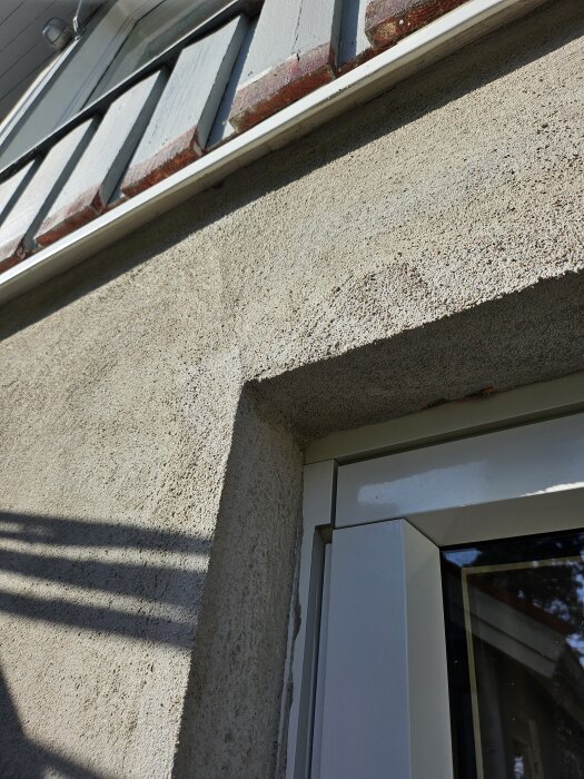 Putsad fasad av souterränghus med slät och grovkornig textur, synliga sprickor vid fönsterkarmar.