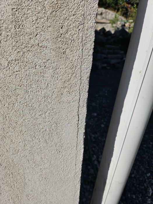 Riven putsad fasad på ett hus med synliga sprickor och ojämn textur. Bakom syns en del av omgivningen.