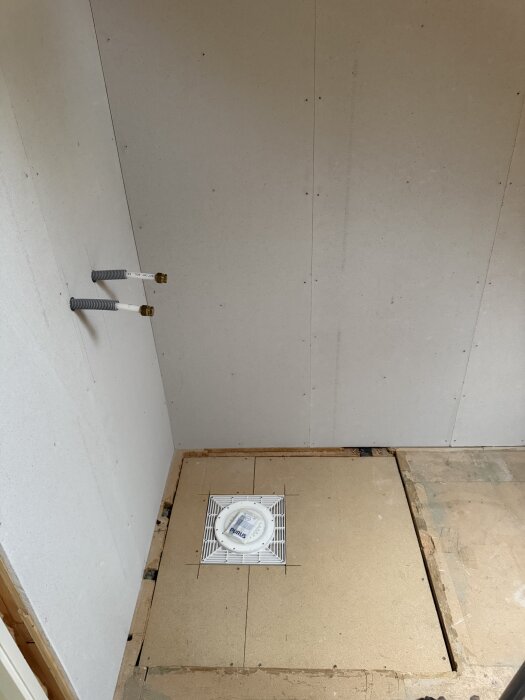 Oavslutat badrum med synliga rör och monterad golvbrunn.