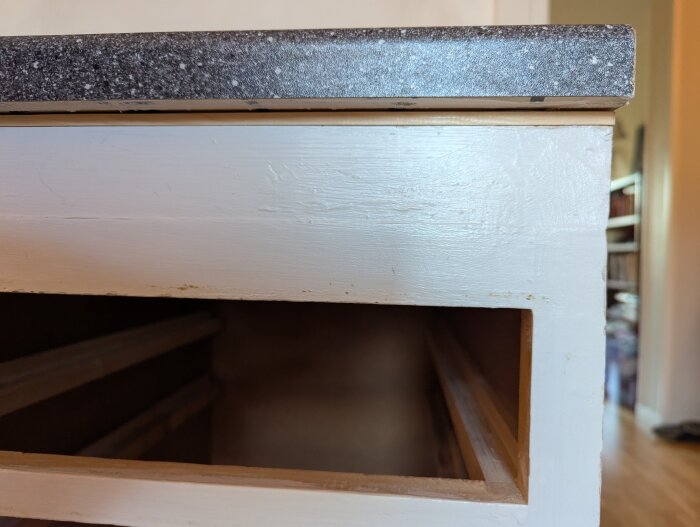 Närbild av ett köksskåps hörn, med vit färg och synlig bänkskiva ovanpå. Listen är fasttejpad mellan skivan och skåpet.