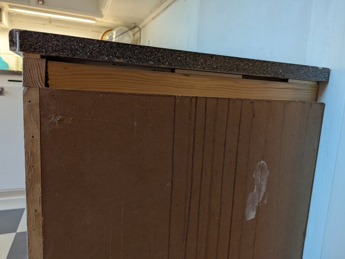Närbild av ett skåp med en avsmalnande list och brun laminerad kortsida, del av gör-det-själv-uppdrag för att räta upp ytan under en bänkskiva.