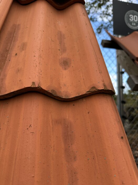 Närbild av enkelkupiga Randers Tegl takpannor, orange i färgen, som visar deras släta yta och djupa kupning.