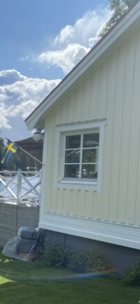Fönster på husgavel med ljusgul fasad och vita foder; svenska flaggan i bakgrunden, diskussion om dekoration och krönlist.