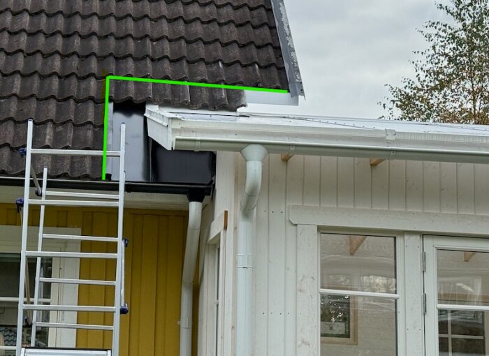 Taket på ett hus med betongpannor har gröna markeringar och en synlig stege vid sidan. En vit hängränna är monterad under taket.