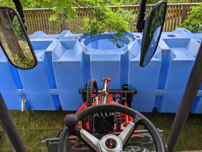 En liten hjullastare syns framför en stor blå behållare i plast, fotograferad från förarens perspektiv.