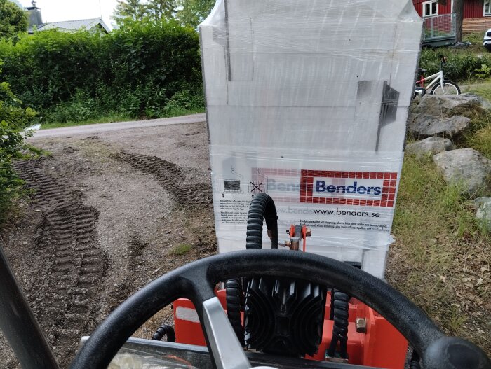 Vy från hytten av en liten elektrisk hjullastare som transporterar en stor pall märkt "Benders", med hjulspår synliga på marken.