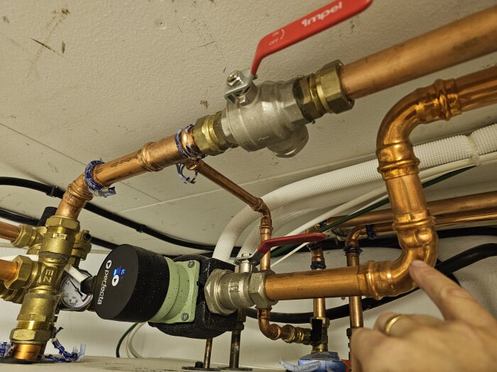 Rörinstallation med kopparrör och ventiler, en hand pekar mot ett rör i ett värmesystem.