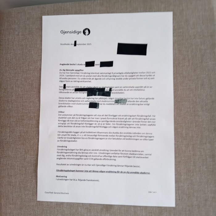 Själva dokumentet från Gjensidige Försäkring som beskriver ett avslagsbeslut med överstrukna delar på en grå tygbakgrund.