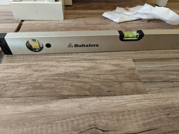 Vattenpass på träplanka visar nivåskillnad mellan gammal och ny del.