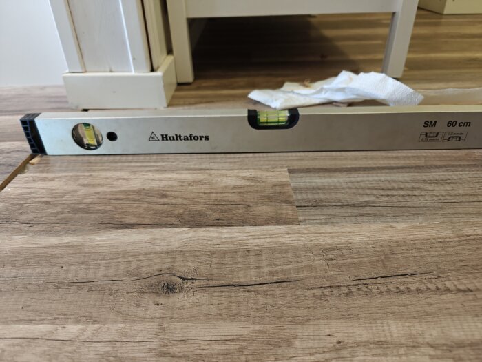 Vattenpass på ett trägolv visar nivåskillnad mellan två delar av golvet.