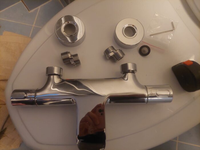 Ny duschblandare med anslutningstillbehör och täckbrickor uppställda på en yta, fotograferad ovanifrån.