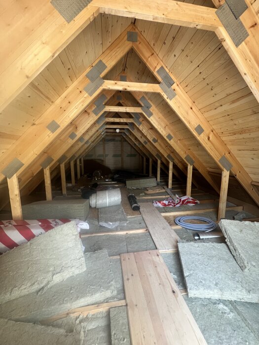 Oinredd övervåning med träpanel och isoleringsmaterial, takstolar synliga, förberedelser för inredning av garage.