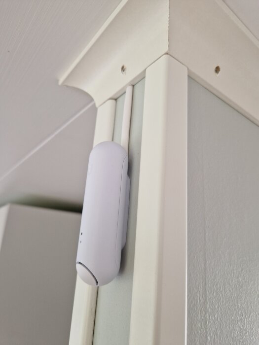 Vit temp/rörelsesensor monterad på en grön vägg nedanför ett vitt tak och smala lister, del av diskussion om PoE och kabeldragningslösningar.