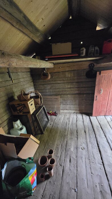 Interiör av ett gammalt uthus med trägolv och timmerväggar; flera föremål, inklusive korgar och rör, ligger på golvet.