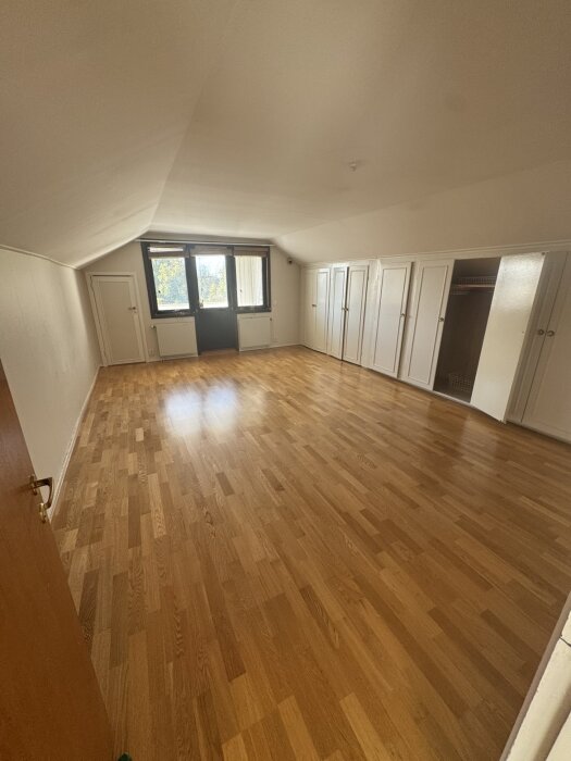 Stor vindsvåning med ekparkettgolv och inbyggda garderober, planerad att delas till två mindre sovrum.